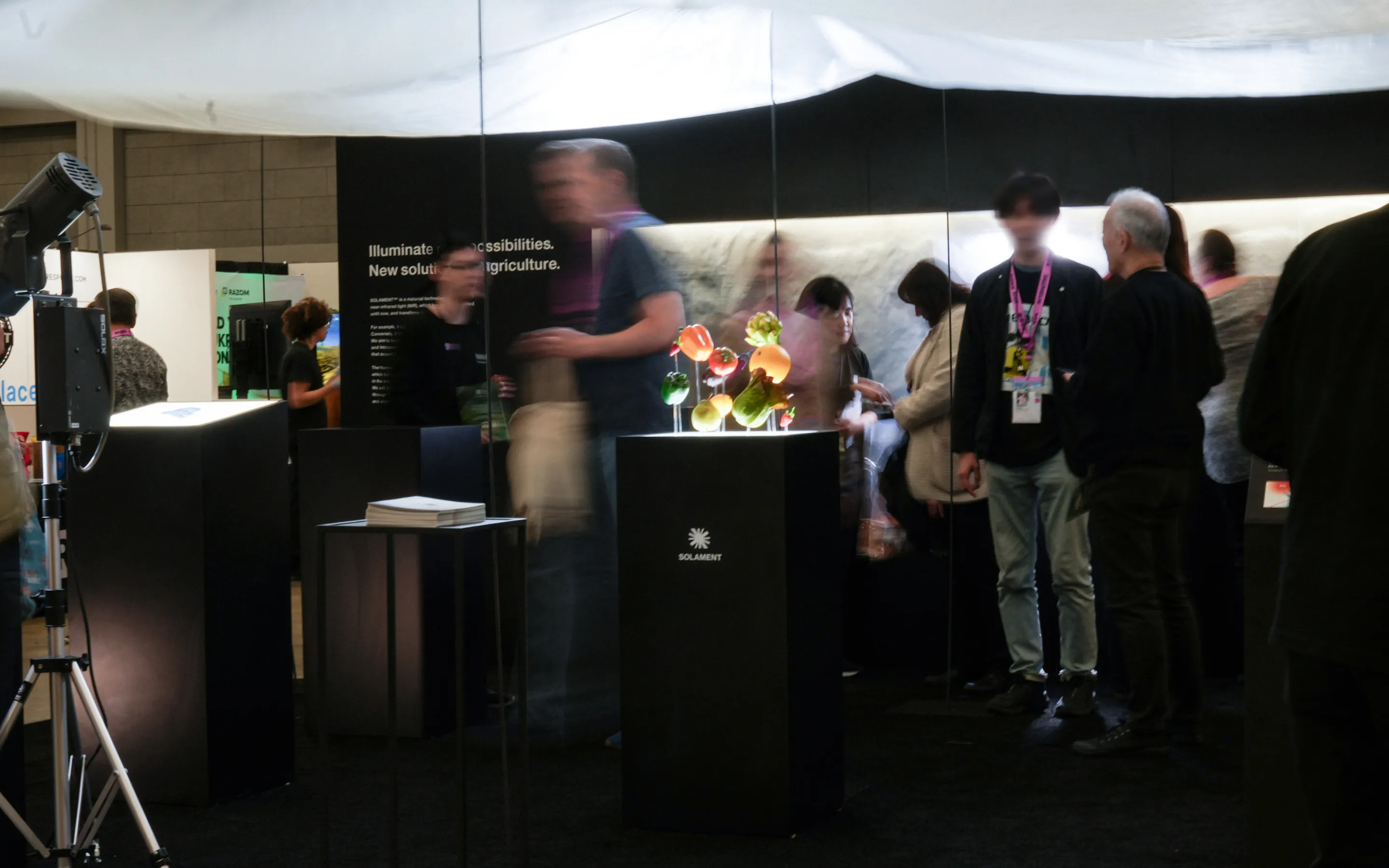 SXSW2025の様子。多くの来場者で賑わう農業向けSOLAMENT®の展示ブース。頭上の白いシェードの下で、ライトアップされた色鮮やかな野菜の展示に見入る人々のビジュアル