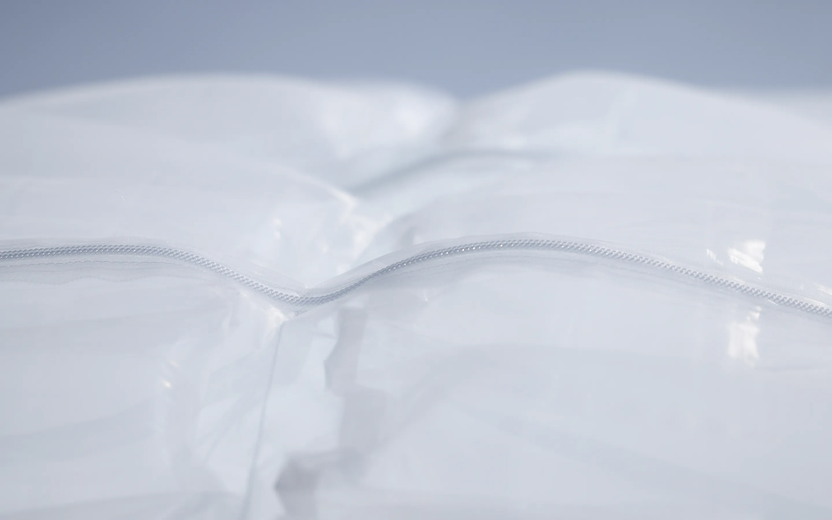 SOLAMENT®（ソラメント）を用いた新しいファッションの形を体現する素材の接写。光を柔らかく反射する白い半透明の素材と、シームレスに閉じたジッパーが、遮熱機能と洗練されたデザイン性を象徴するメインビジュアル。
