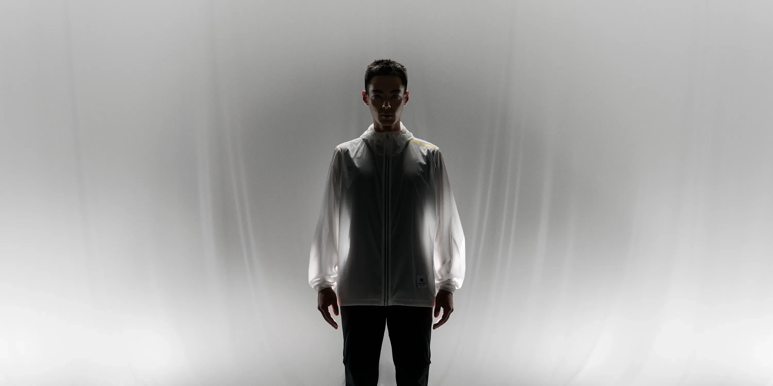 背後からの強い光の中に立つ男性。CROSS-DOOR JACKETが白く輝き、その生地の薄さと心地よい発熱機能を表現。