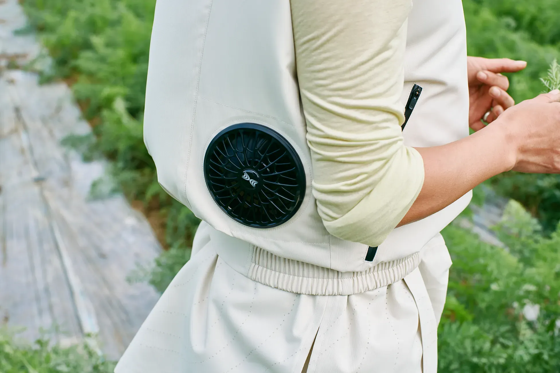 農地を背景に、ファン（扇風機）付きのベージュの農作業用ベスト（HOPE WEAR for Farm Type B）を着用した人物の腰回りのクローズアップ。