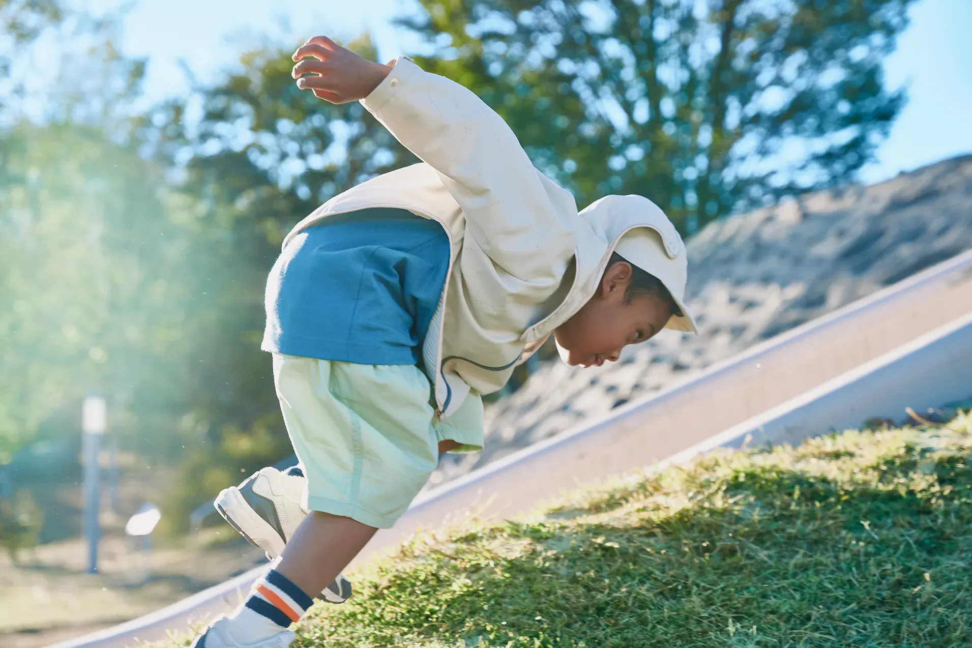 プリーツジャケット（HOPE WEAR for Play）を着て外遊びをする男の子。プリーツが風を取り込んで広がる様子。