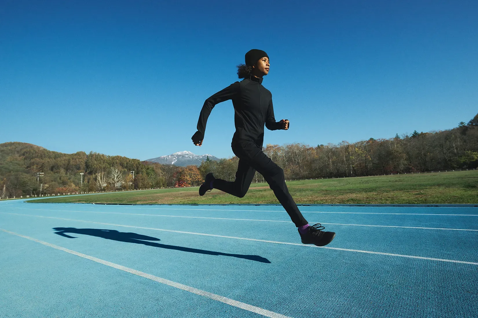 山々を望むトラックを疾走する女性。SOLAR-PERFORMANCE WEARで、寒冷環境でのパフォーマンス維持することを表現。
